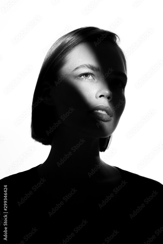Fototapeta premium Fashionable beauty portrait. Black silhouette on white background. Girl with a spot of light on her face. 