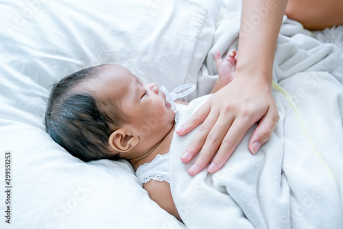 Asian newborn baby is sleeping on white bed with mother hand put on her chest to take care and make her feel safe.