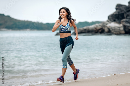 Fit smiling girl is running across the sandy beach of the Andaman sea, welness concept