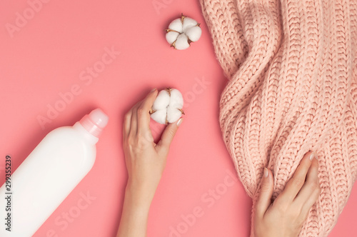 Eco cleaning concept. White plastic packaging of laundry detergent, liquid powder, washing conditioner, knitted wool sweater, cotton flowers on pink background. Flat lay top view. Bio organic product