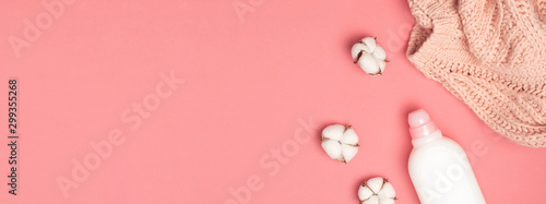 Eco cleaning concept. White plastic packaging of laundry detergent, liquid powder, washing conditioner, knitted wool sweater, cotton flowers on pink background. Flat lay top view. Bio organic product
