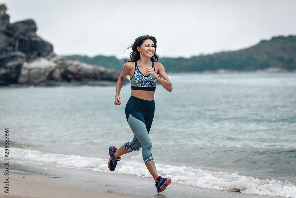 Fit smiling girl is running across the sandy beach of the Andaman sea, welness concept Fit smiling girl is running across the sandy beach of the Andaman sea, welness concept