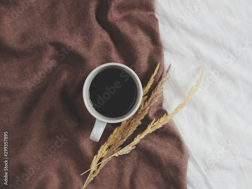 Cup of coffee isolated on white linen background surrouned by big brown scarf. Flat lay. Top view. Copy space photo