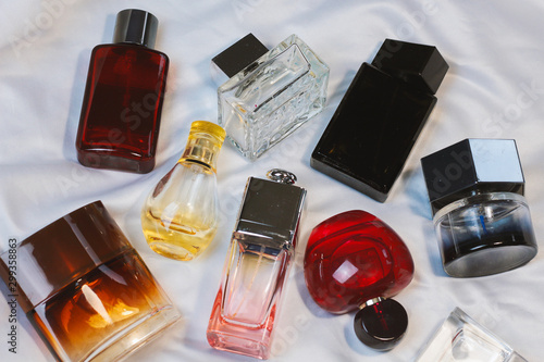Colorful fashion trendy bottles of perfume toilet water fragrances  lie on a silver gray sheet on the bed, top view. Female and male fragrances 