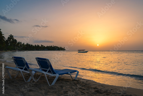 Two beach chairs and boat background on the tropical beach at sunset Dominican republic Bahia Principe beach.