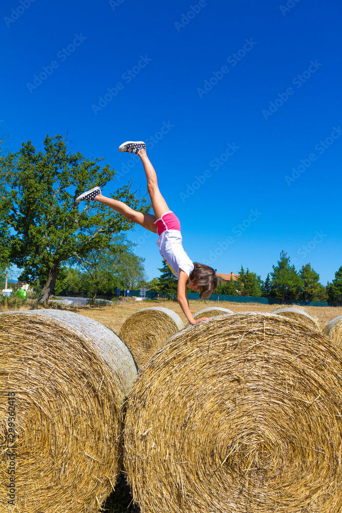Girl performs a somersault on hay bales in the middle of the countryside near Florence Girl performs a somersault on hay bales in the middle of the countryside near Florence