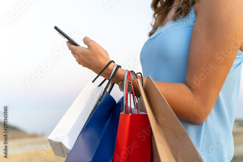 Young woman using her mobile phone with some shopping bags. Shopping concept