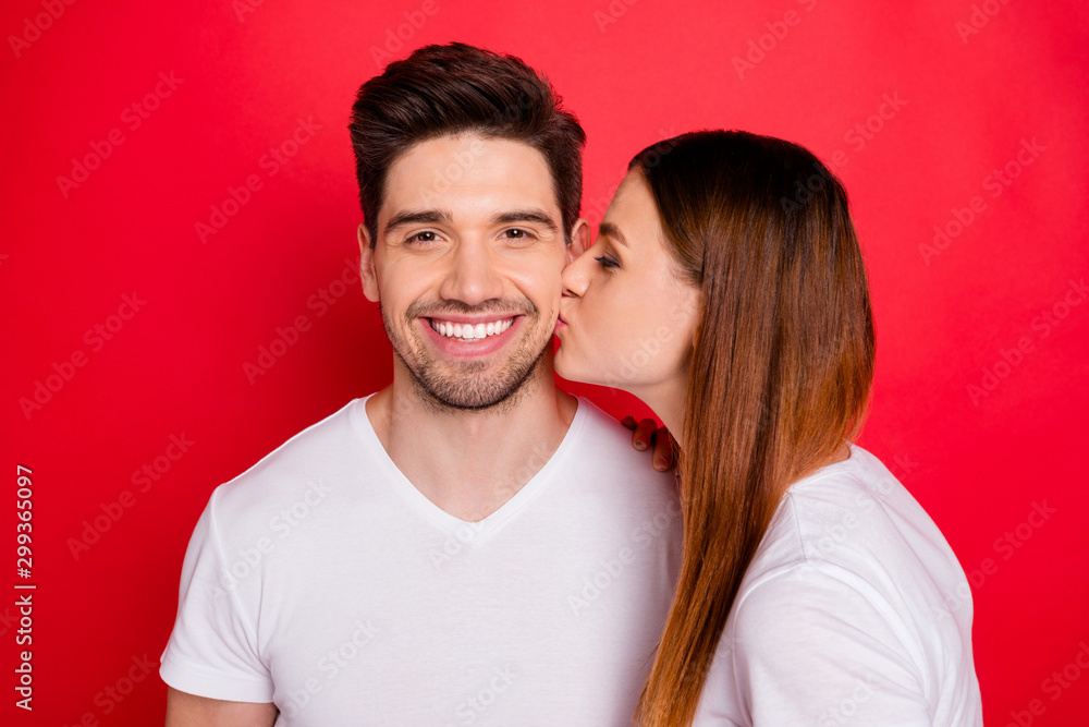 Photo of redhair positive cute nice pretty couple of married people with wife in white t-shirt kissing her husband cheek smiling toothily showing their tender love isolated bright red color background Photo of redhair positive cute nice pretty couple of married people with wife in white t-shirt kissing her husband cheek smiling toothily showing their tender love isolated bright red color background