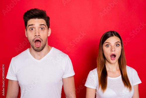Photo of scared atonished couple of friends afraid of fake bad news spreading with mouth open wide expressing fear on faces with stubble on male face white t-shirt isolated vivid color background