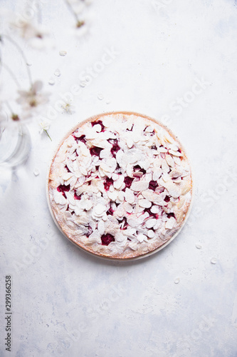 Whole cherry cake with almond petals and sugar powder on white background with cherry flowers.