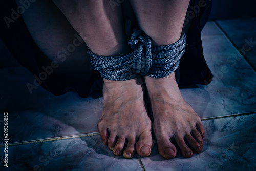 A woman suffers from violence. Female legs tied with a rope.