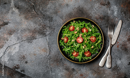 Healthy vegetable salad of fresh arugula, tomato and walnut on dark plate. Diet menu. Top view. Salad with arugula