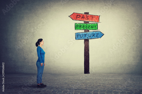 Konstfotografi Side view of young woman standing in front of a signpost with arrows shows past, present and future