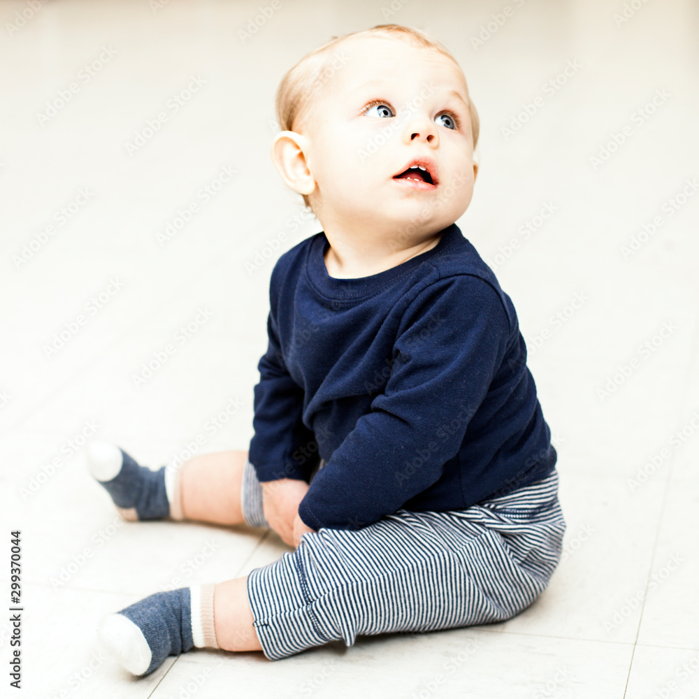 Concentrated little boy sitting and looking away. Baby boy wearing blue sweater and striped pants. Newborn childhood, childhood - obrazy, fototapety, plakaty 