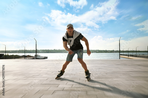 Handsome young man roller skating on pier near river