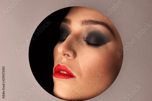 Beauty portreai of a woman with gorgeus makeup thwough circle in gray background photo