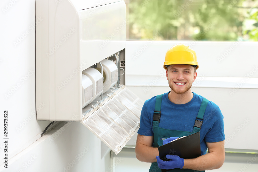 Professional technician with clipboard near modern air conditioner indoors Professional technician with clipboard near modern air conditioner indoors