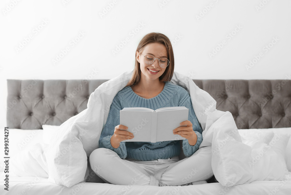 Young woman in warm sweater reading book on bed at home Young woman in warm sweater reading book on bed at home