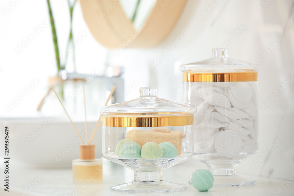 Jars with cotton pads and bath bombs on white countertop in bathroom Jars with cotton pads and bath bombs on white countertop in bathroom