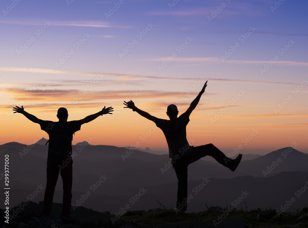 backlit hikers in celebration gesture. Tourist high on the top of a mountain at sunset looking towards the landscape.