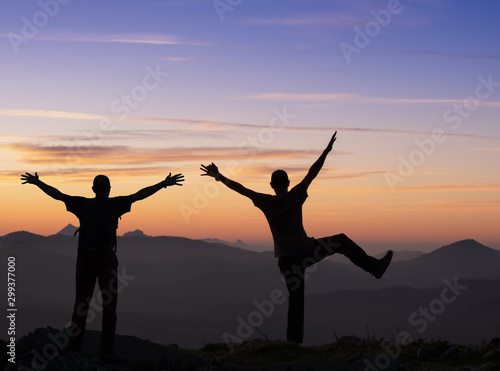 Fototapeta Naklejka Na Ścianę i Meble -  backlit hikers in celebration gesture. Tourist high on the top of a mountain at sunset looking towards the landscape.