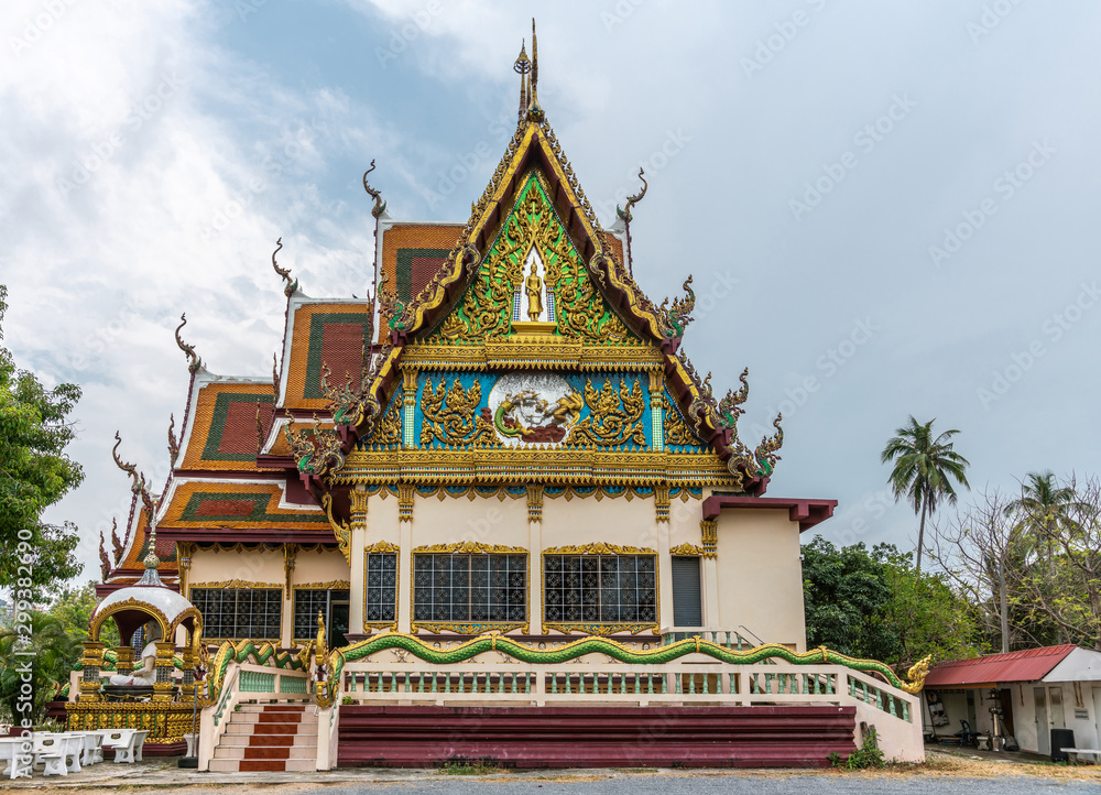 Fototapeta premium Ko Samui Island, Thailand - March 18, 2019: Wat Laem Suwannaram Chinese Buddhist Temple. Elaborately decorated full of colors north side facade under blue cloudscape and green foliage.