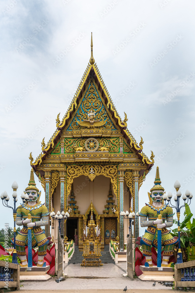 Ko Samui Island, Thailand - March 18, 2019: Wat Laem Suwannaram Chinese Buddhist Temple. Entrance to Wat Plai Laem shrine with two dwarapalaka statues up front, and golden facade and gable.