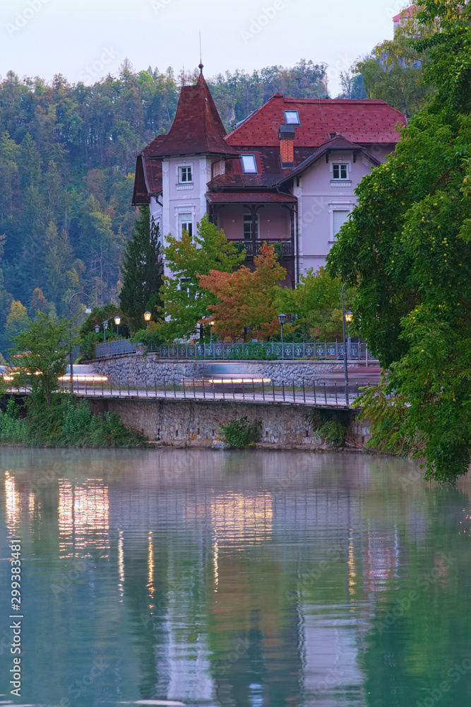 Scenic morning view of ancient traditional house near Bled lake. Morning fog on the water surface and fall colorful trees background. Bled Lake, the Upper Carniolan region of northwestern Slovenia