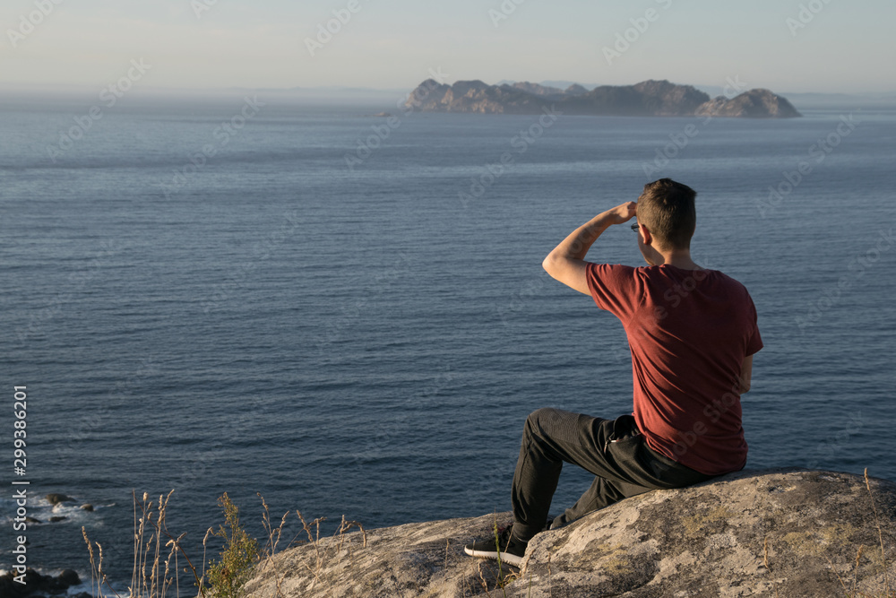 Man covering his face looking at the ocean sitting on a rock