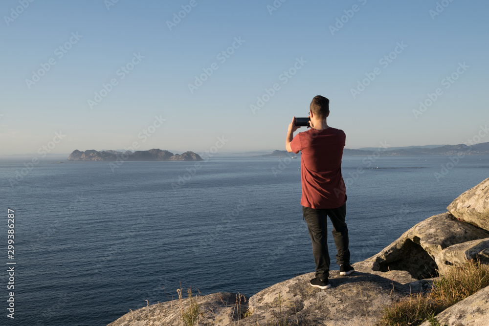 Rear view of a boy taking a photo of the sea from the mountain