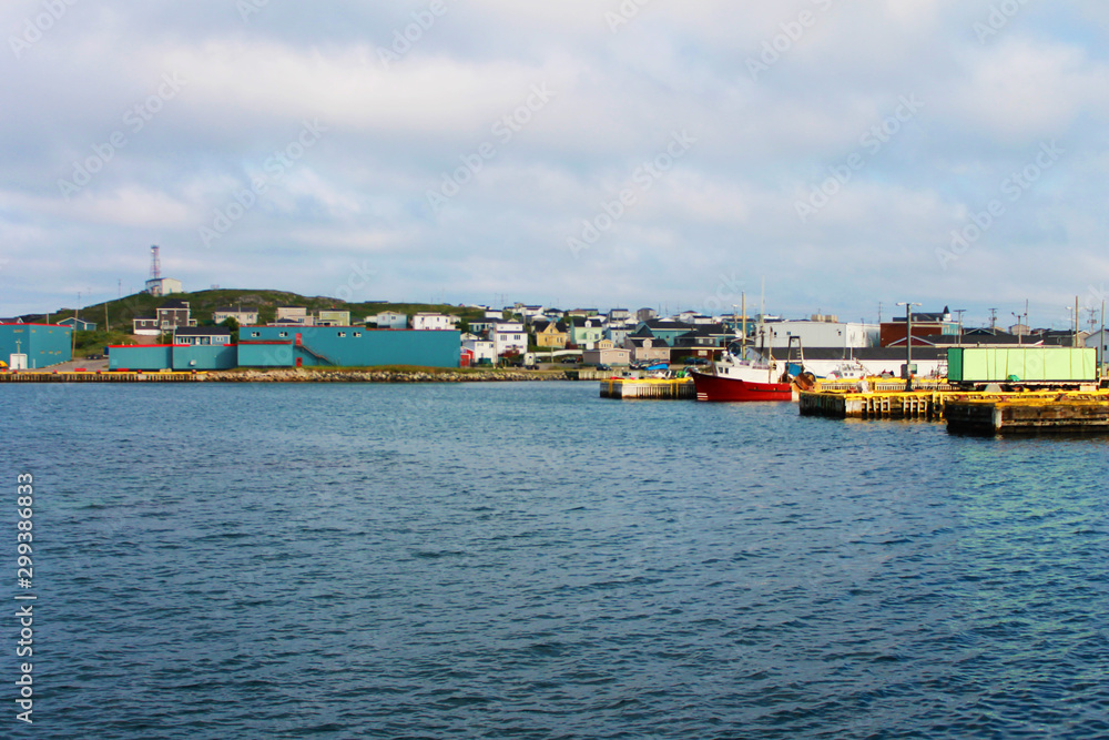 Looking in toward the town of Port-aux-Basque, Newfoundland Labrador, from the harbour. Commercial buildings on the waterfront, boats on the dock, houses on the hill.