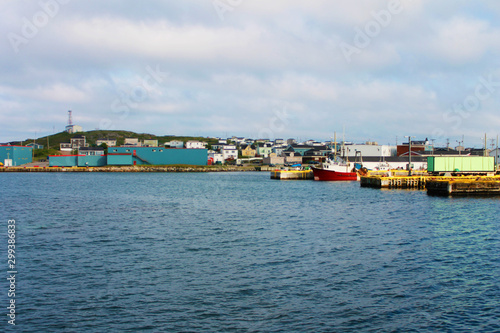 Looking in toward the town of Port-aux-Basque, Newfoundland Labrador, from the harbour. Commercial buildings on the waterfront, boats on the dock, houses on the hill.