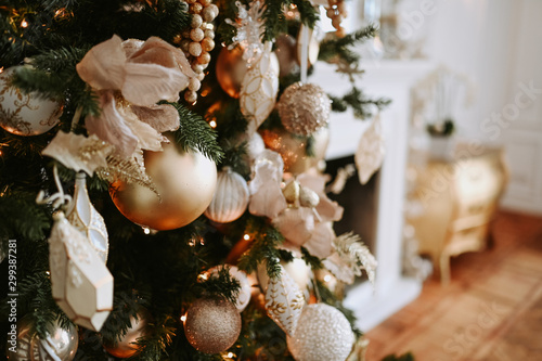 A fragment of a Christmas decorated tree in warm golden hues on a brurred white classic room interior background . New Year and Christmas concept. Festive postcard photo