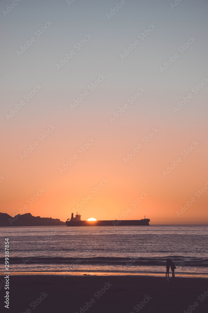 Couple facing the sea on a sunset with the sun hiding behind a boat