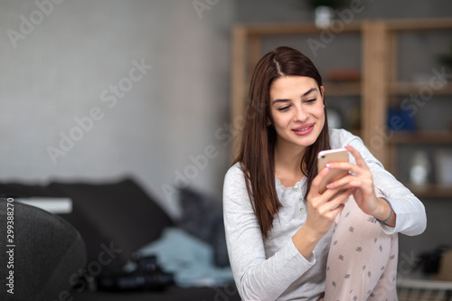 Beautiful young girl in pijama in living room use mobile phone and smile
