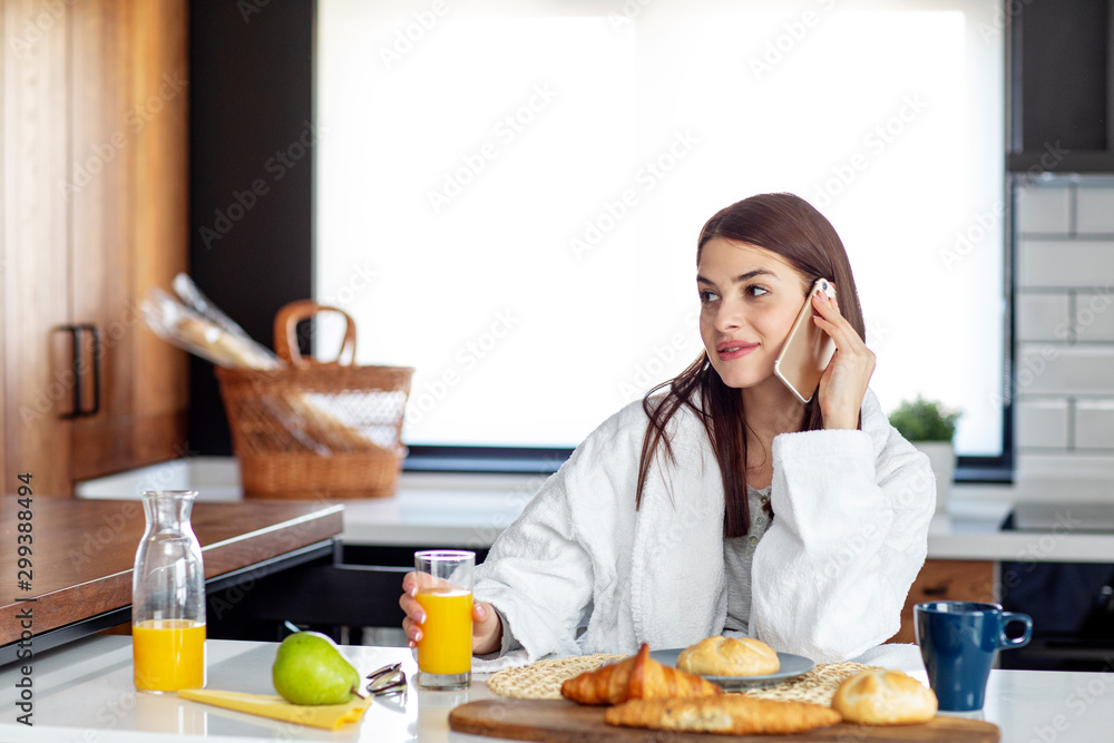 With breakfast at the kitchne with pastry and orange juice on table young woman start in the morning using mobile phone With breakfast at the kitchne with pastry and orange juice on table young woman start in the morning using mobile phone