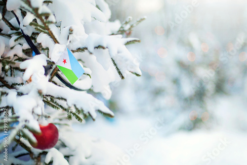 Christmas Djibouti. Xmas tree covered with snow, decorations and flag. Snowy forest background in winter. Christmas greeting card. © theartofpics