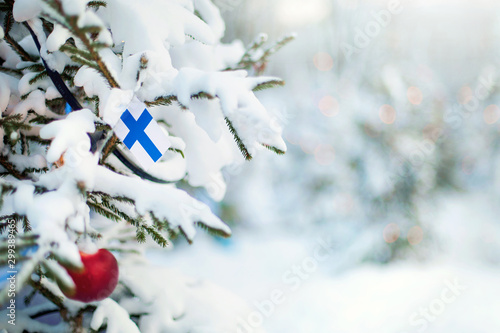 Christmas Finland. Xmas tree covered with snow, decorations and Finnish flag. Snowy forest background in winter. Christmas greeting card. 2021 New Year