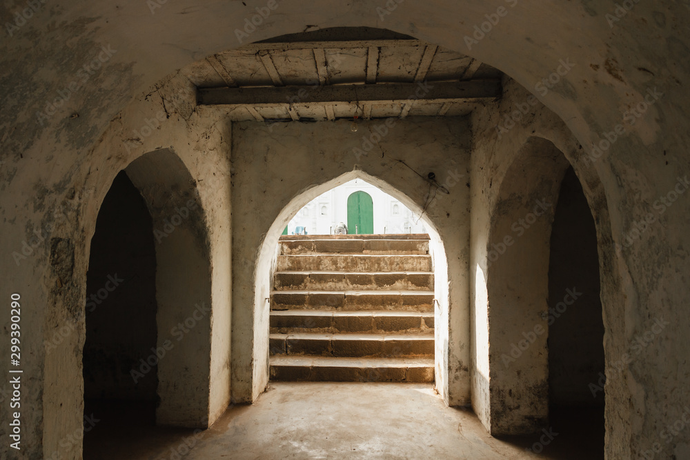 Naklejka premium Murshidabad, West Bengal/India - January 15 2018: The elegant symmetry of the arches, stairs and architectural detail inside an old mosque in Murshidabad.