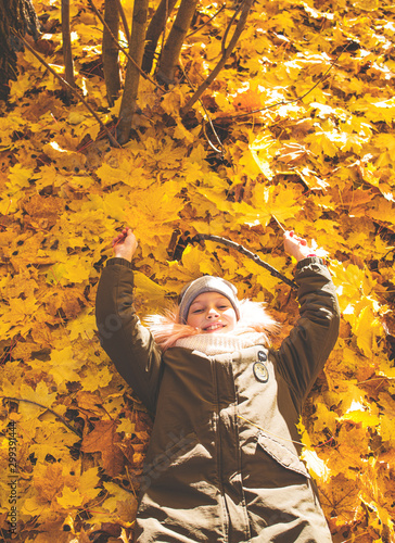 Funny girl lies on yellow leaves in the forest. Child on a walk in the autumn park. Young girl on the street