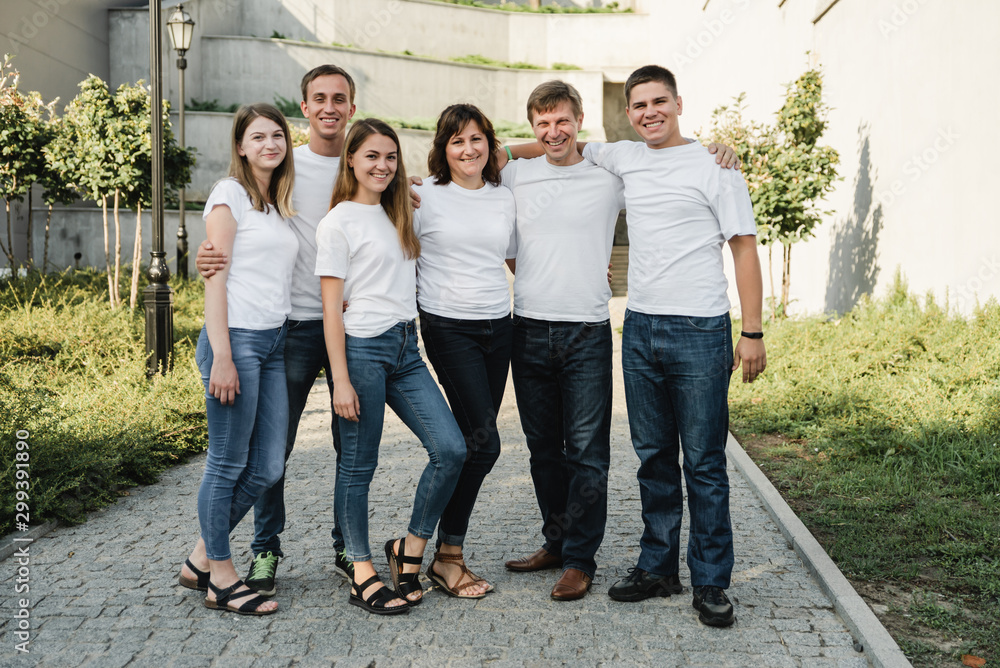 Obraz premium Happy family in white T-shirt and jeans emracing and having fun. Parents with their adult children walking in the park. Family time concept