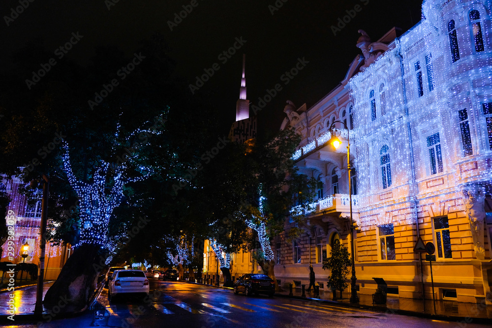 Illuminated trees in night street. New Year in Batumi, Georgia. City with New Years decorations. Neon lights and holiday trees decorated with glowing Christmas lights 