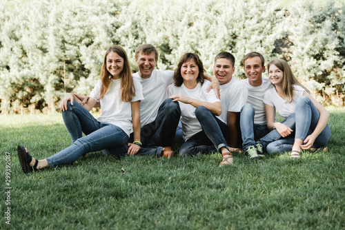 Happy family in white T-shirt and jeans sitting on the green grass. Parents with their adult children walking in the park. Family time concept