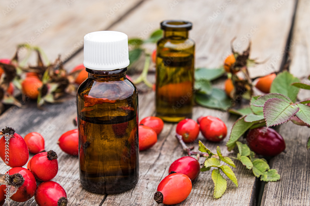 Bottle of rosehip seed essential oil and fresh red berries on a wooden table. Tincture or essential oil with rose hips. Bottle of rosehip seed essential oil and fresh red berries on a wooden table. Tincture or essential oil with rose hips.