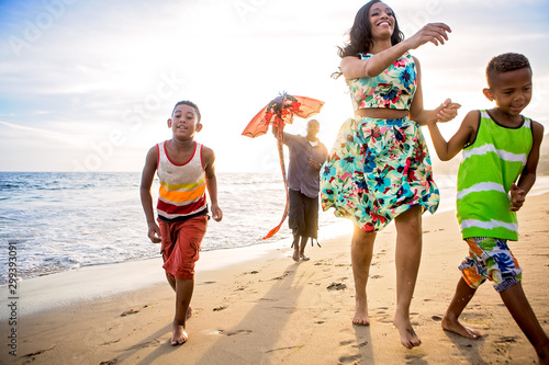 Family flying a kite on the beach at sunset wearing casual clothes