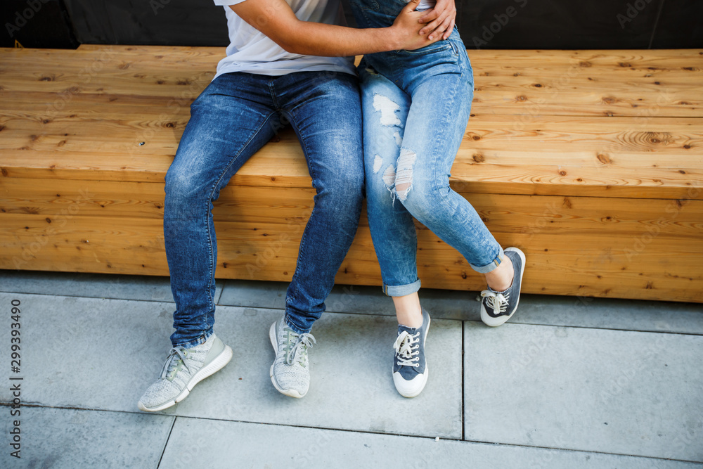 A young couple is sitting on a bench in a modern city, hugging and smiling.