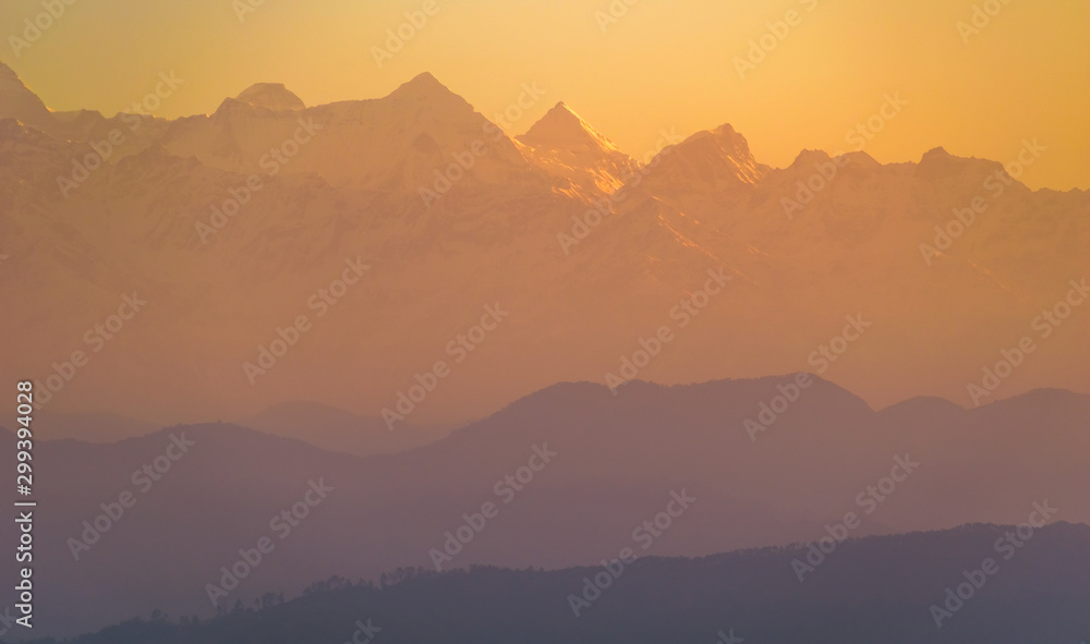 The yellow-orange morning light hits the scenic Himalayan peaks in the Indian town of Kausani in Kumaon in the state of Uttarakhand, India.