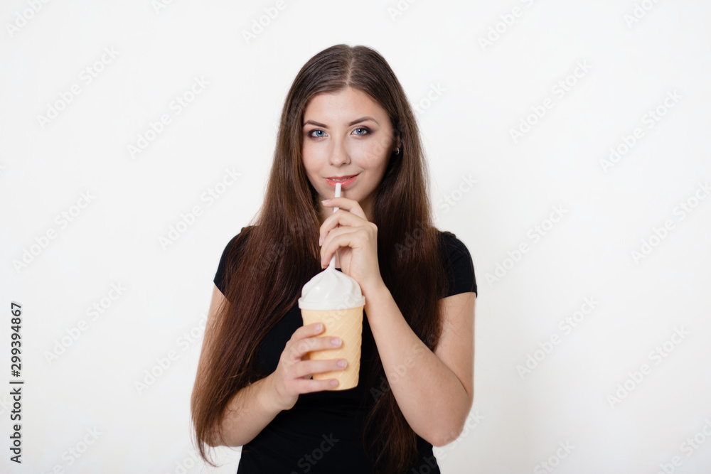 A young, beautiful girl in a black T-shirt and blue jeans is holding a glass with a straw in her hands. Studio photo on white background. A young, beautiful girl in a black T-shirt and blue jeans is holding a glass with a straw in her hands. Studio photo on white background.