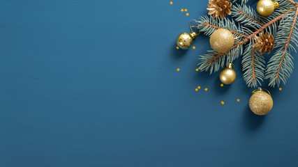 Christmas composition with green pine branch, golden decorations and balls, confetti on blue background with copy space. Top view, Flat lay. Xmas banner mockup, vintage postcard template