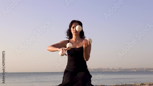 beautiful young woman juggles balls on the sea beach. Evening sun